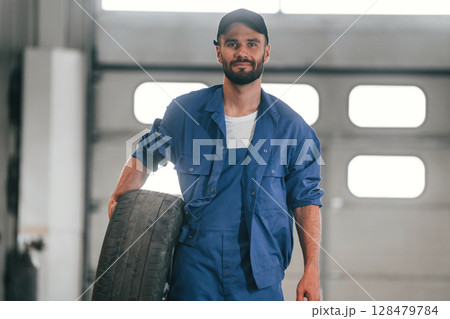 Tire in hand. Auto mechanic working in garage. Repair service 128479784