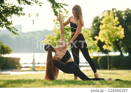 Teaching how to do exercises. Two women in sport clothes are doing exercises outdoors on the field 128480167