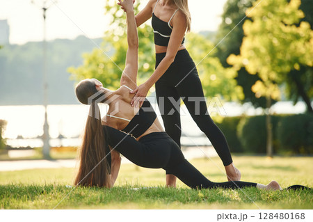 Teaching how to do exercises. Two women in sport clothes are doing exercises outdoors on the field 128480168