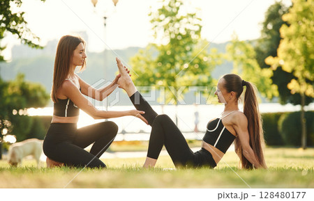 Teaching the new exercises. Two women in sport clothes are doing exercises outdoors on the field Teaching the new exercises. Two women in sport clothes are doing exercises outdoors on the field 128480177