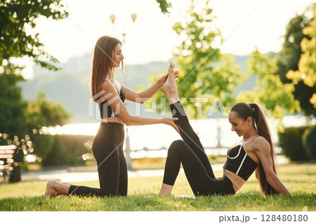 Teaching the new exercises. Two women in sport clothes are doing exercises outdoors on the field 128480180