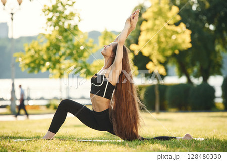 On the yoga mat. Beautiful young woman in sportive clothes is in the park at sunny daytime 128480330