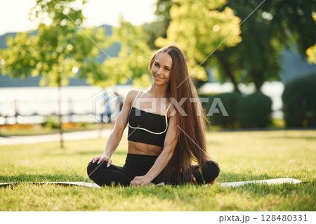 On the yoga mat. Beautiful young woman in sportive clothes is in the park at sunny daytime 128480331