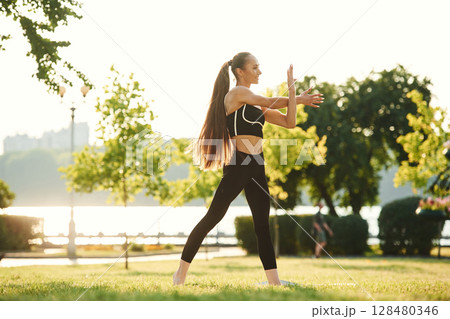 Warming up hands. Beautiful young woman in sportive clothes is in the park at sunny daytime Warming up hands. Beautiful young woman in sportive clothes is in the park at sunny daytime 128480346