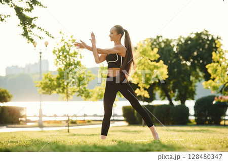 Warming up hands. Beautiful young woman in sportive clothes is in the park at sunny daytime Warming up hands. Beautiful young woman in sportive clothes is in the park at sunny daytime 128480347