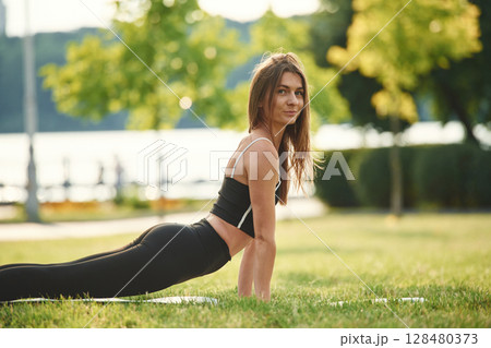 Exercises for the spine. Beautiful young woman in sportive clothes is in the park at sunny daytime 128480373