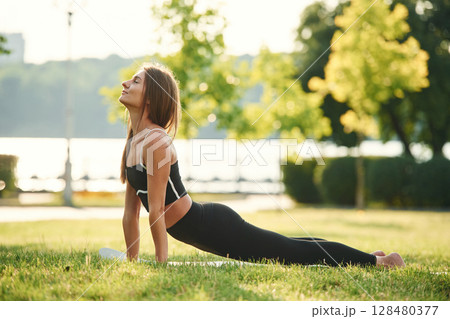 Exercises for the spine. Beautiful young woman in sportive clothes is in the park at sunny daytime Exercises for the spine. Beautiful young woman in sportive clothes is in the park at sunny daytime 128480377