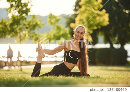 Leg stretching. Beautiful young woman in sportive clothes is in the park at sunny daytime Leg stretching. Beautiful young woman in sportive clothes is in the park at sunny daytime 128480469