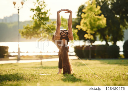 Muscular arms. Beautiful young woman in sportive clothes is in the park at sunny daytime 128480476