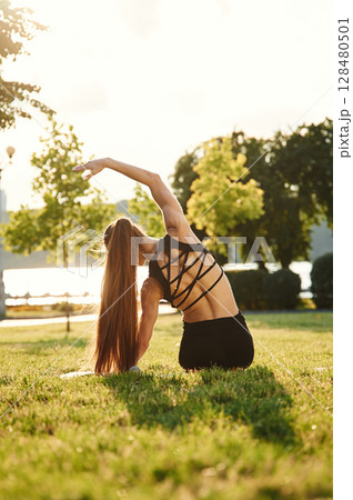 View from the back, sitting. Beautiful young woman in sportive clothes is in the park at sunny daytime 128480501