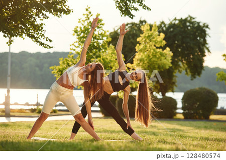 Two women in sport clothes are doing exercises outdoors on the field 128480574
