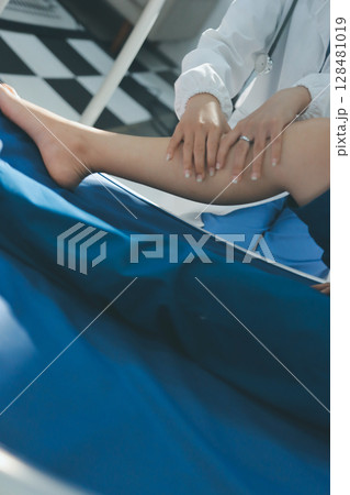 Female doctor hands doing physical therapy By extending the leg and knee of a male patient 128481019