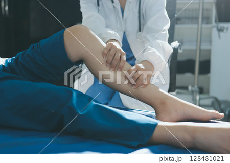 Female doctor hands doing physical therapy By extending the leg and knee of a male patient 128481021