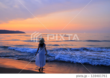 夕暮れの波打ち際を歩く女性 夕暮れの波打ち際を歩く女性 128481761