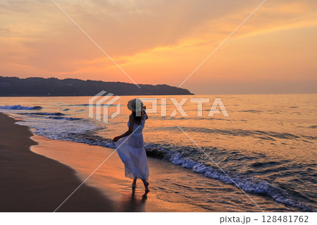夕暮れの波打ち際を歩く女性 夕暮れの波打ち際を歩く女性 128481762