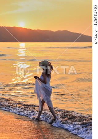 夕暮れの波打ち際を歩く女性 夕暮れの波打ち際を歩く女性 128481765