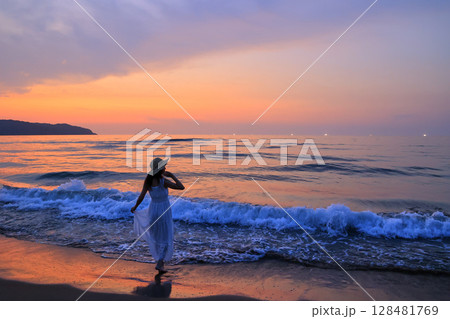 夕暮れの波打ち際を歩く女性 128481769