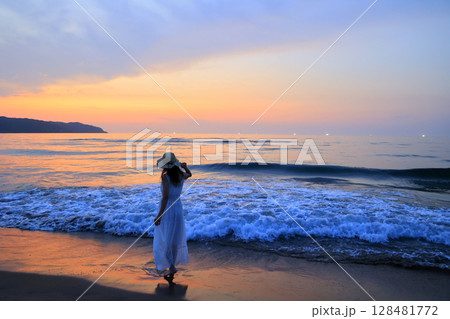 夕暮れの波打ち際を歩く女性 128481772
