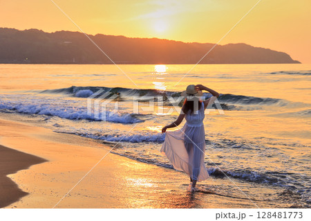 夕暮れの波打ち際を歩く女性 夕暮れの波打ち際を歩く女性 128481773
