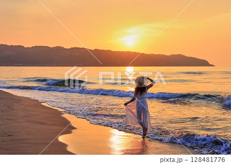 夕暮れの波打ち際を歩く女性 夕暮れの波打ち際を歩く女性 128481776