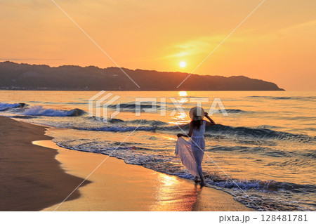 夕暮れの波打ち際を歩く女性 128481781