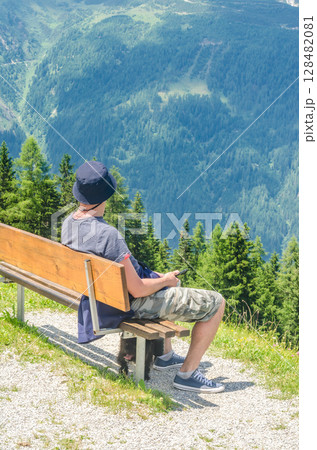 Man Relaxing on Bench Overlooking Forested Alpine Valley with Dog Resting Below. High quality photo Man Relaxing on Bench Overlooking Forested Alpine Valley with Dog Resting Below. High quality photo 128482081