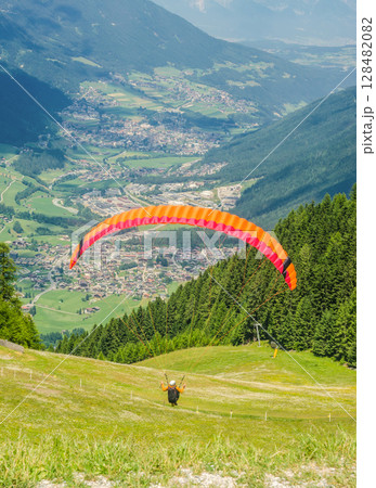 Colorful Paraglider Taking Off Above Alpine Valley and Scenic Village Below. High quality photo 128482082