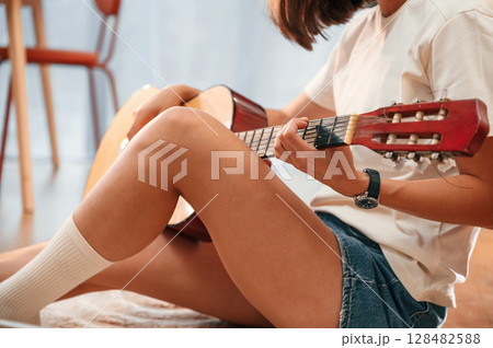 With classical guitar in hands. Beautiful woman in casual clothes is at home in domestic room 128482588