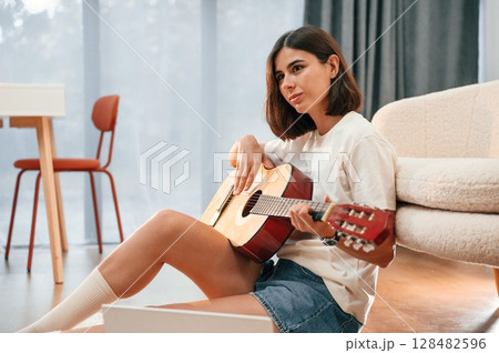 Learning to play classical guitar. Beautiful woman in casual clothes is at home in domestic room 128482596