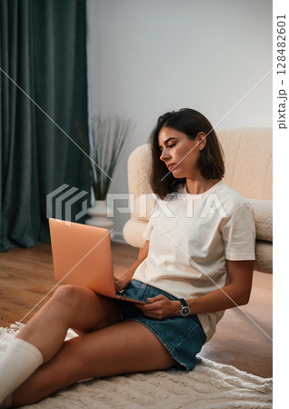 With laptop that is on the legs. Beautiful woman in casual clothes is at home in domestic room With laptop that is on the legs. Beautiful woman in casual clothes is at home in domestic room 128482601