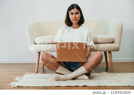 Sitting on the floor and using laptop. Beautiful woman in casual clothes is at home in domestic room 128482609