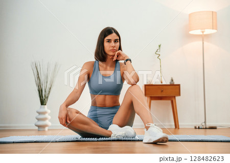On yoga mat. Pretty woman in sportive clothes have fitness day indoors 128482623