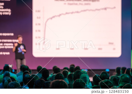 Conference audience watching a presentation with charts on a large screen Conference audience watching a presentation with charts on a large screen 128483150