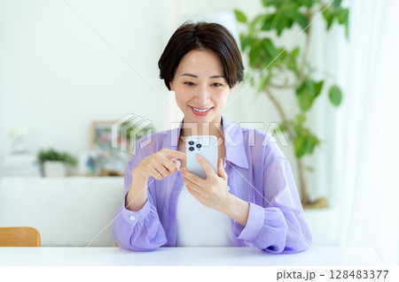 部屋でスマホを操作するミドル女性 128483377