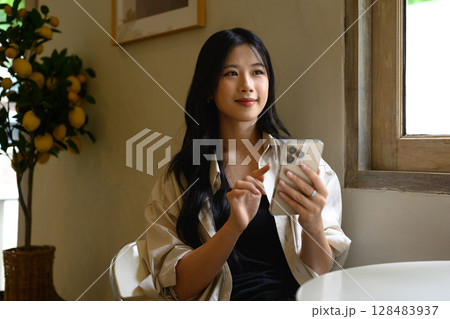 Pretty young woman using smartphone by the window in a cozy cafe Pretty young woman using smartphone by the window in a cozy cafe 128483937