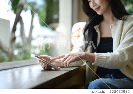 Close up of woman hands using smartphone by a cafe window Close up of woman hands using smartphone by a cafe window 128483956
