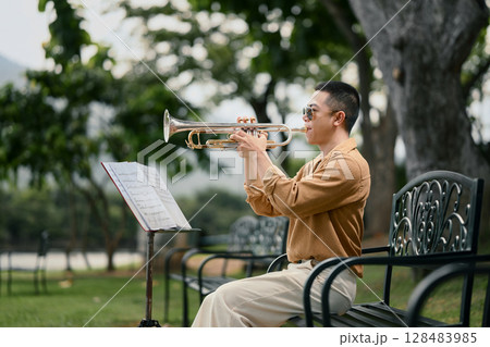 Musician reading sheet music while performing trumpet in a peaceful garden 128483985