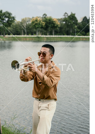 Male musician enjoying a solo trumpet performance by serene lakeside Male musician enjoying a solo trumpet performance by serene lakeside 128483994