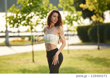 Standing and posing. Beautiful young woman in sportive clothes is in the park at sunny daytime 128484271