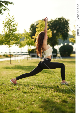 Side view. Beautiful young woman in sportive clothes is in the park at sunny daytime Side view. Beautiful young woman in sportive clothes is in the park at sunny daytime 128484322