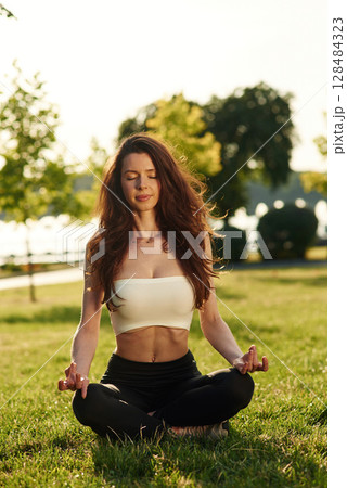 Peaceful meditation. Beautiful young woman in sportive clothes is in the park at sunny daytime Peaceful meditation. Beautiful young woman in sportive clothes is in the park at sunny daytime 128484323