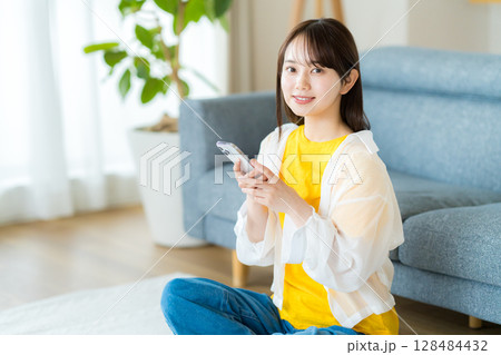 部屋でスマホを操作する若い女性 128484432