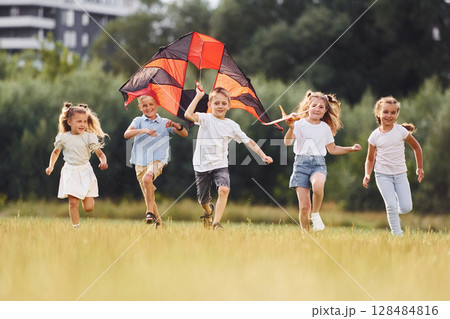Running together. Group of kids are running and playing with kite on green field 128484816