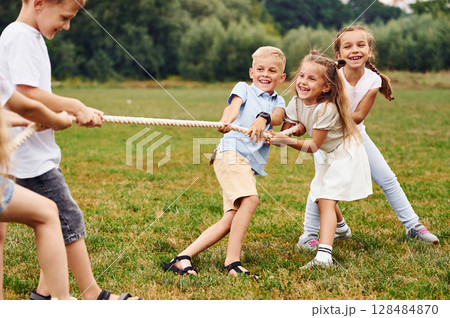 Playing tug of war game. Kids are having fun on the field at daytime together Playing tug of war game. Kids are having fun on the field at daytime together 128484870