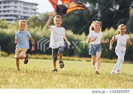 Running together. Group of kids are running and playing with kite on green field 128484897