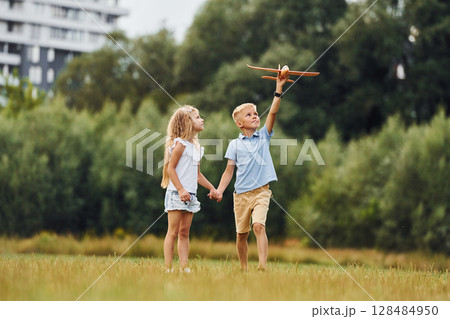 Boy and girl are playing with toy plane on the green field 128484950