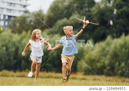 Boy and girl are playing with toy plane on the green field 128484951