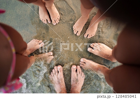 Family enjoying a sunny day at the beach with playful toes in the sand 128485041