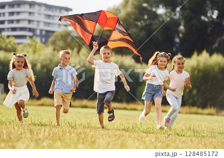 Running together. Group of kids are running and playing with kite on green field 128485172