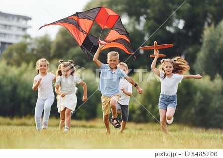 Happy children. Group of kids are running and playing with kite on green field 128485200